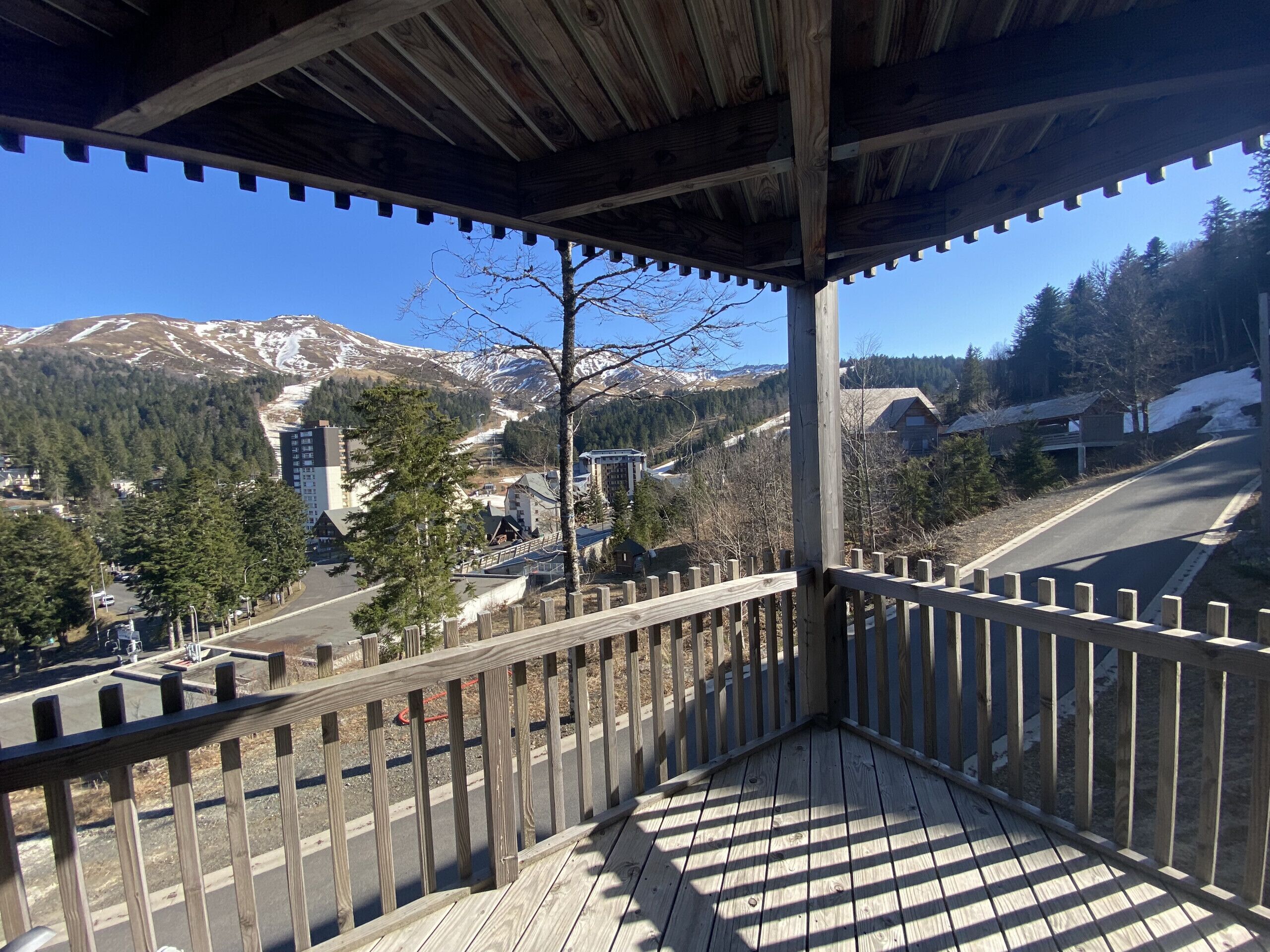A wooden balcony with a view of a mountain range and a town below.
