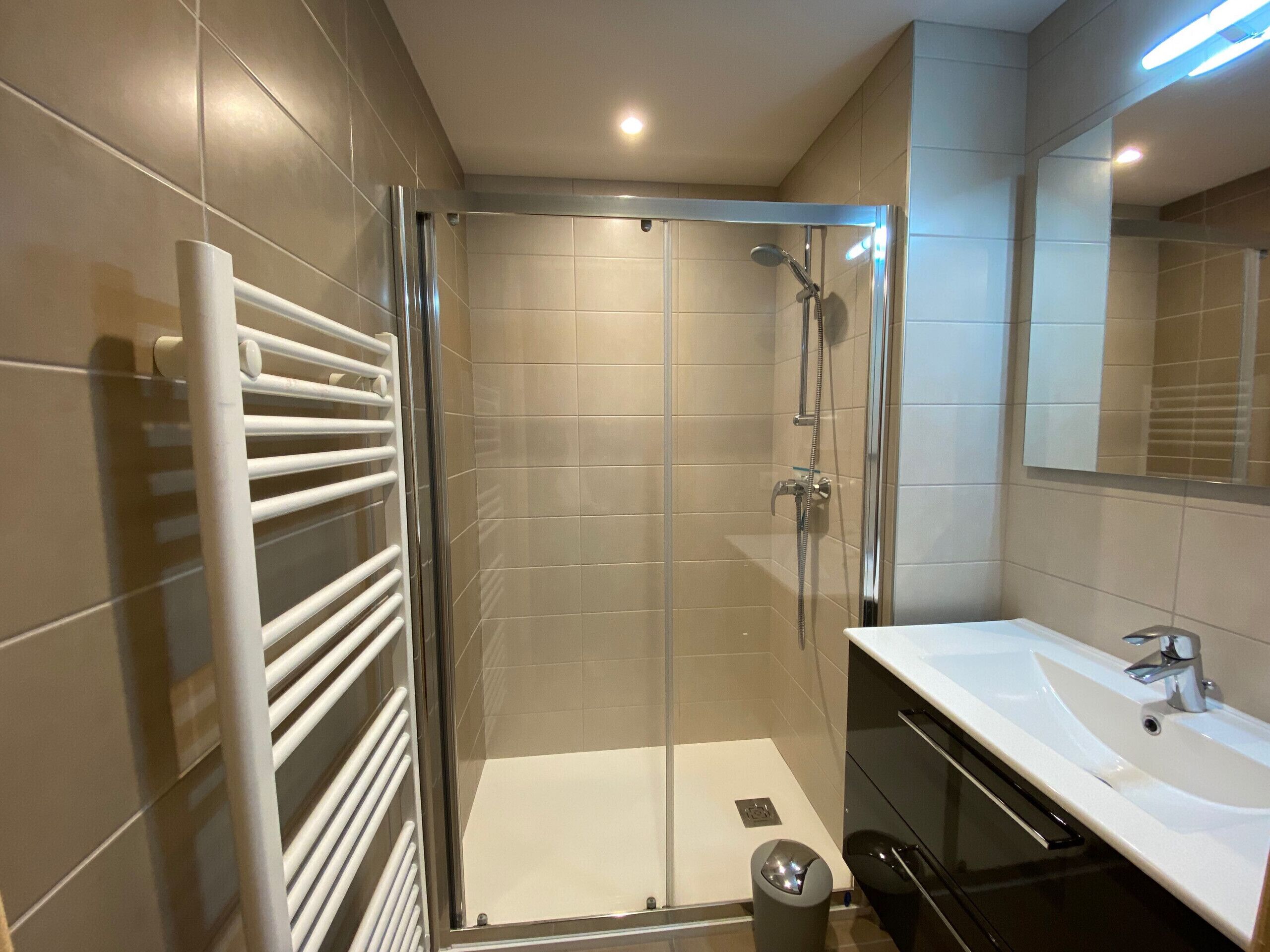 Een moderne badkamer met een douchecabine van glas, een wit wastafelmeubel en een grote spiegel.