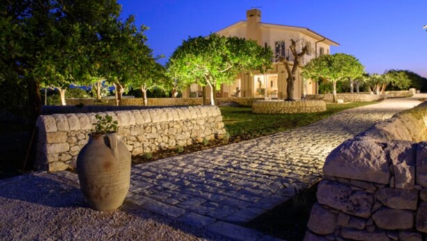 A stone pathway leading to a building with a stone wall on one side and trees on the other.