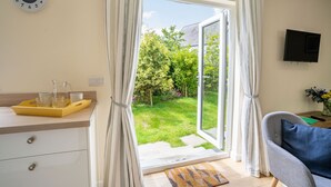 Una stanza con una porta scorrevole in vetro che dà su un giardino, un orologio appeso al muro e una TV montata.