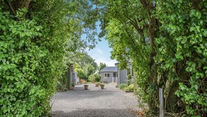 En grusvej fører til et hus omgivet af frodig vegetation.