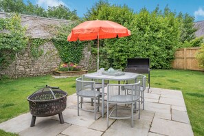 A patio with a round table, four chairs, a grill, and a fire pit. - Caldey Lodge (Tenby)