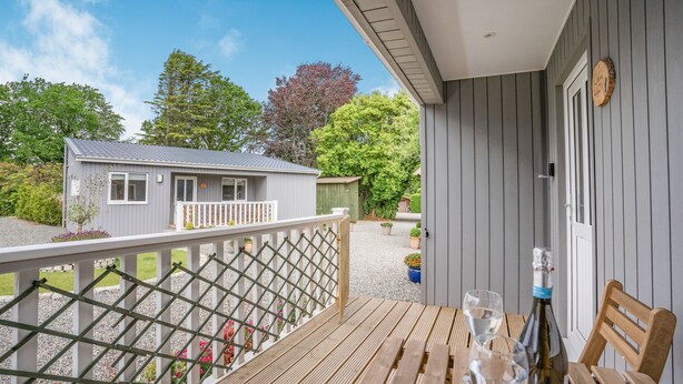 En træterrasse med et bord og stole, en vinflaske og et glas på bordet.