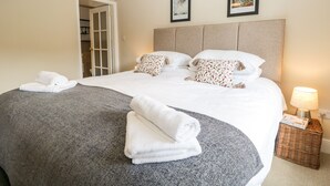 Cama bem arrumada com lençóis brancos e almofadas decorativas, um abajur e um quadro na parede.