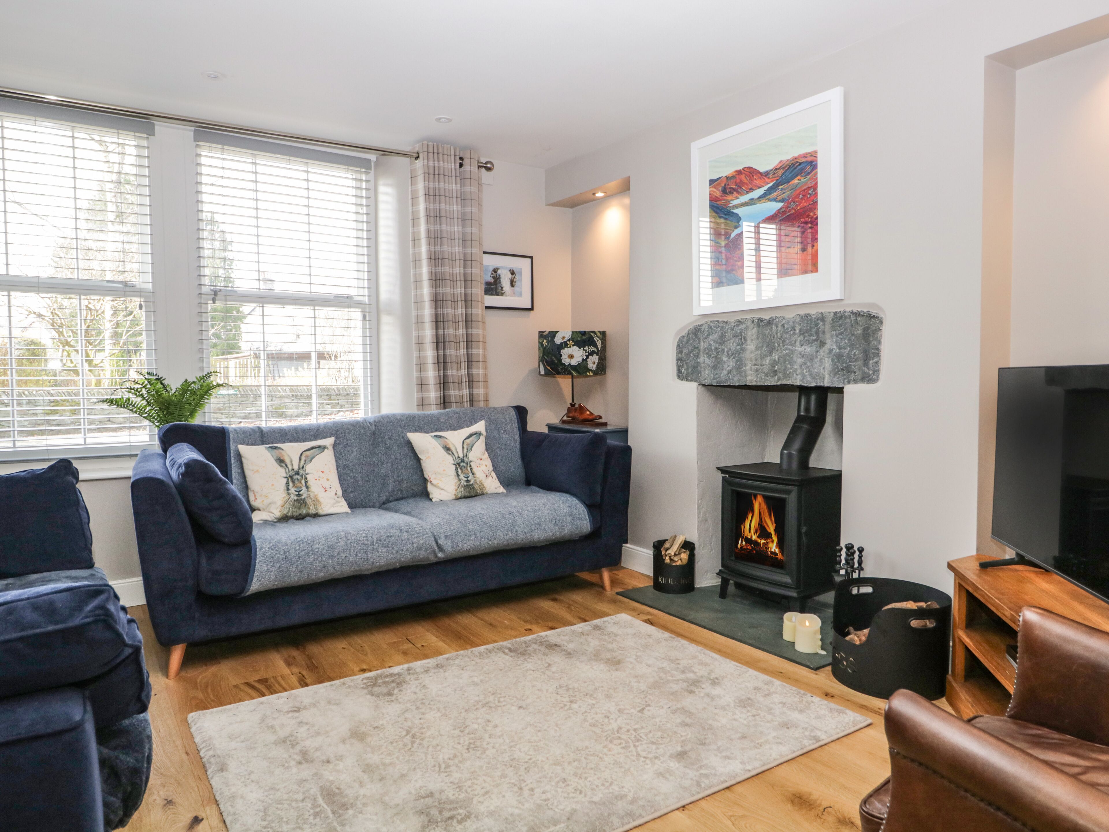 Una sala de estar moderna con un sofá azul, una chimenea, un televisor y un ventanal con persianas.
