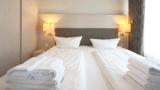 Habitación de hotel con dos camas, cada una con ropa blanca y toallas, y dos lámparas fijadas a la pared.