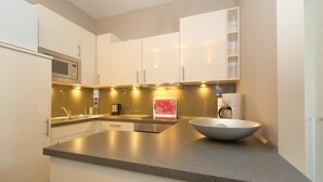 Una cocina moderna con armarios blancos, microondas de acero inoxidable, una isla grande con un bol y luces debajo de los armarios.
