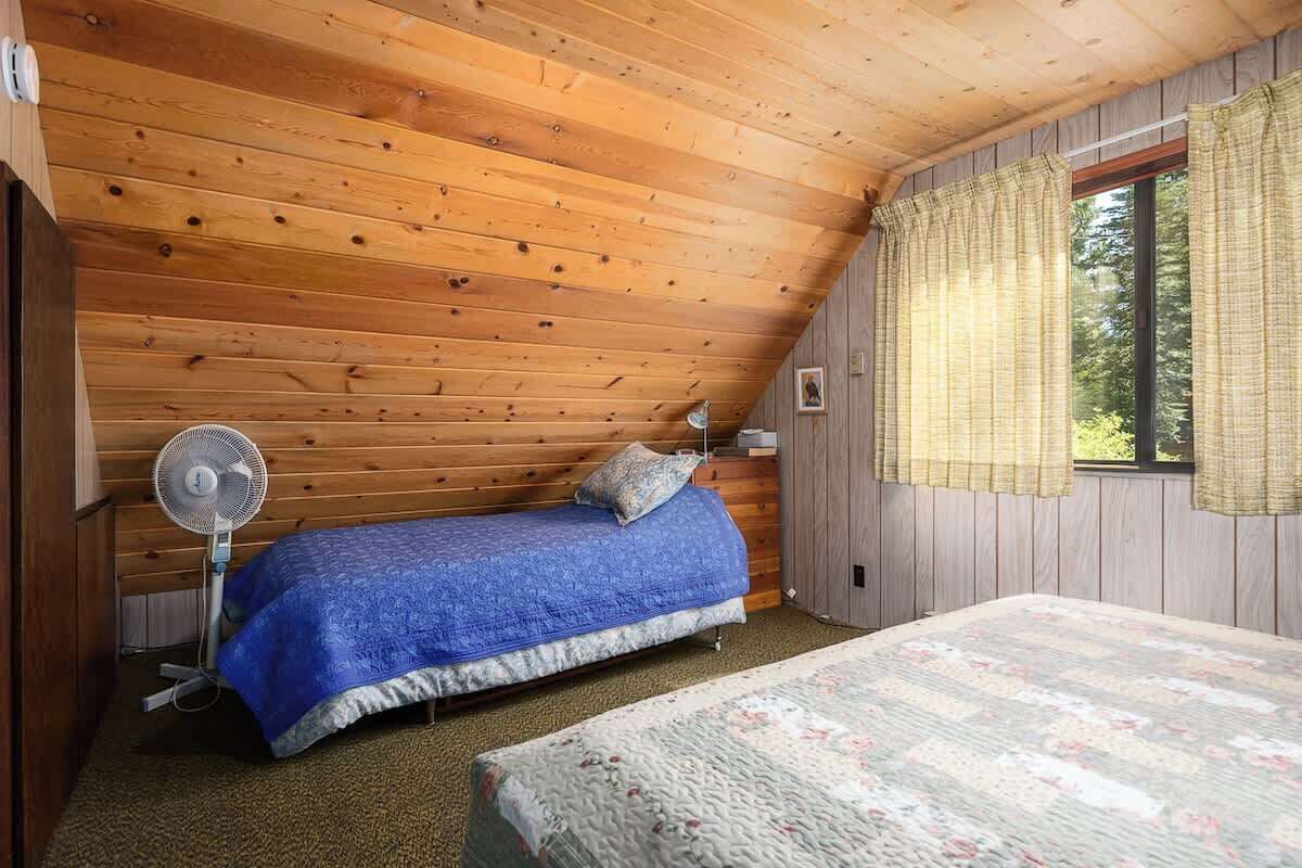 Une cabane avec une chambre à coucher aménagée en mezzanine, un lit, un ventilateur et une fenêtre avec des rideaux.