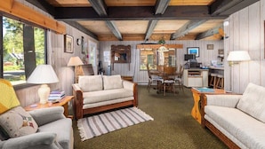 A cozy cabin interior with a wooden ceiling, a dining area, and a kitchenette.