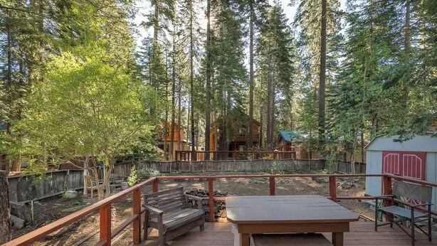 A wooden deck with a table and benches, surrounded by a wooden fence and tall trees.
