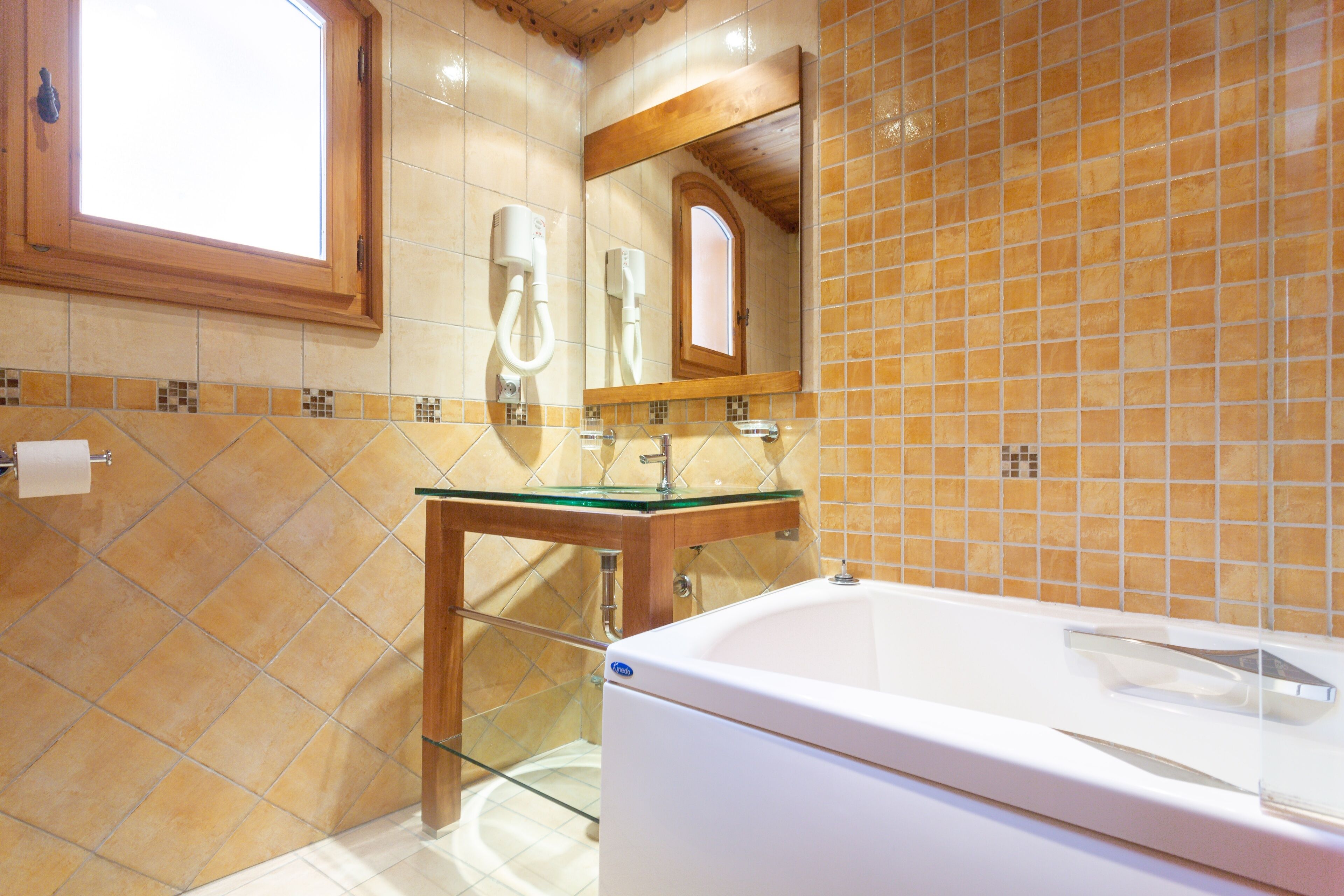A modern bathroom with a glass-enclosed sink, a white bathtub, and a tiled wall with a window above the mirror.