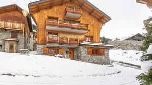 Un chalet en bois, avec une base en pierre, des balcons en bois et un pont de pierre en arrière-plan.