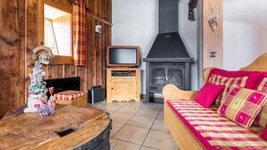 Une pièce chaleureuse avec des murs en bois, une cheminée, une télévision et un lit agrémenté d’une literie aux couleurs vives.