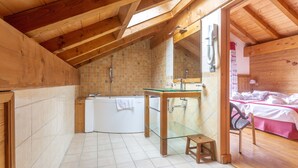 Un intérieur en bois avec un lavabo protégé par une paroi de verre, une baignoire et un lit avec des serviettes.