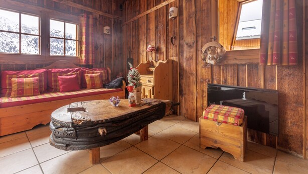 L’intérieur d’un chalet accueillant, avec un banc en bois, une petite table et une fenêtre donnant sur des montagnes enneigées.