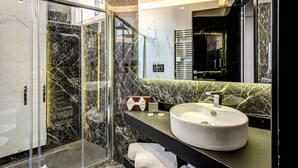 Een moderne badkamer met een glazen douchecabine, een groot wastafelmeubel met een marmeren blad en een spiegel met een zwarte lijst.