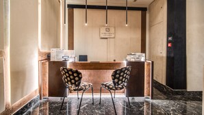 Een receptiehal met een marmeren vloer, twee gestreept patroon stoelen, een houten receptiebalie en een bord met daarop 'DORIA PALACE HOTEL & CONDOMINIUM'.