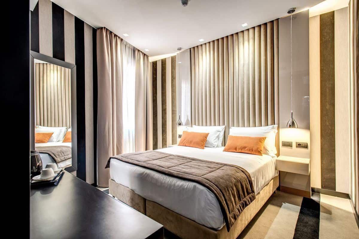Une chambre d’hôtel moderne avec un grand lit, une table de chevet, un miroir et une vue sur le paysage urbain.