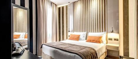 A modern hotel room with a large bed, a bedside table, a mirror, and a view of the cityscape.