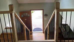 A spacious room with a sloped ceiling, a skylight, a wooden staircase with black railings, and a door leading outside.