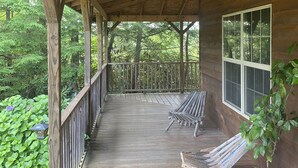 A wooden porch with two lounge chairs, a potted plant, and a stone birdbath.