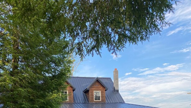 A wooden house with a covered porch, a chimney, and a gravel driveway.