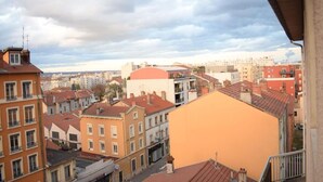 Uma paisagem urbana com diversos edifícios, incluindo um edifício laranja proeminente em primeiro plano e um edifício com telhado vermelho ao fundo.