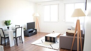 Uma sala de estar moderna com área de jantar, televisão de tela plana e luminária de pé.