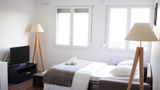 Quarto moderno com cama, mesas de cabeceira, televisão e abajur.