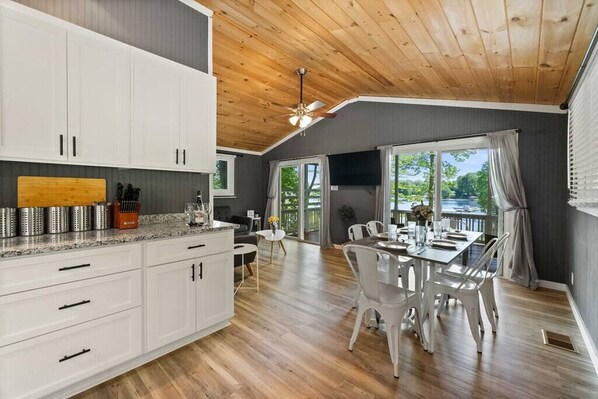 A modern kitchen with white cabinets, a granite countertop, and a dining area with a table and chairs.