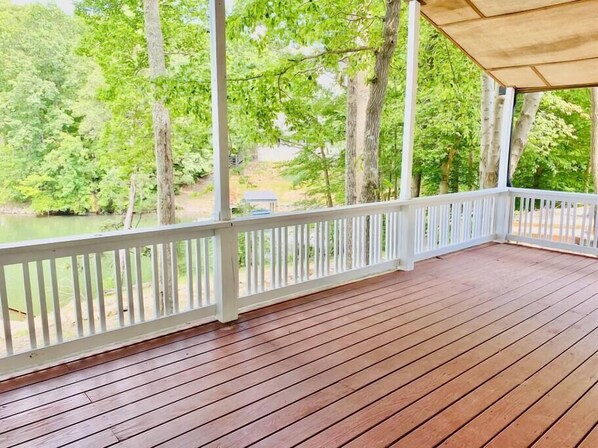 A wooden deck with white railings overlooking a body of water and trees.
