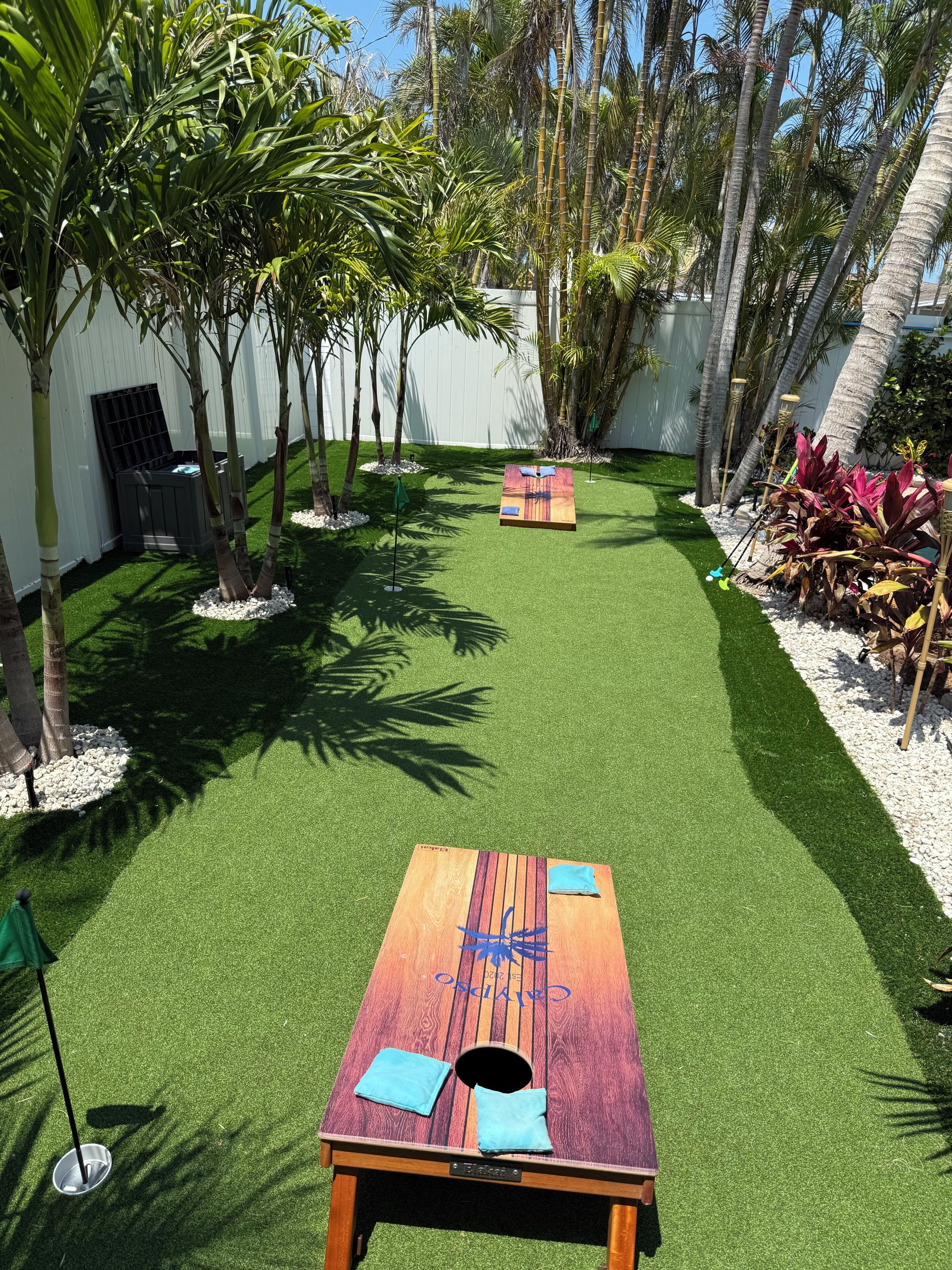 A backyard with artificial grass, a wooden table, and palm trees.