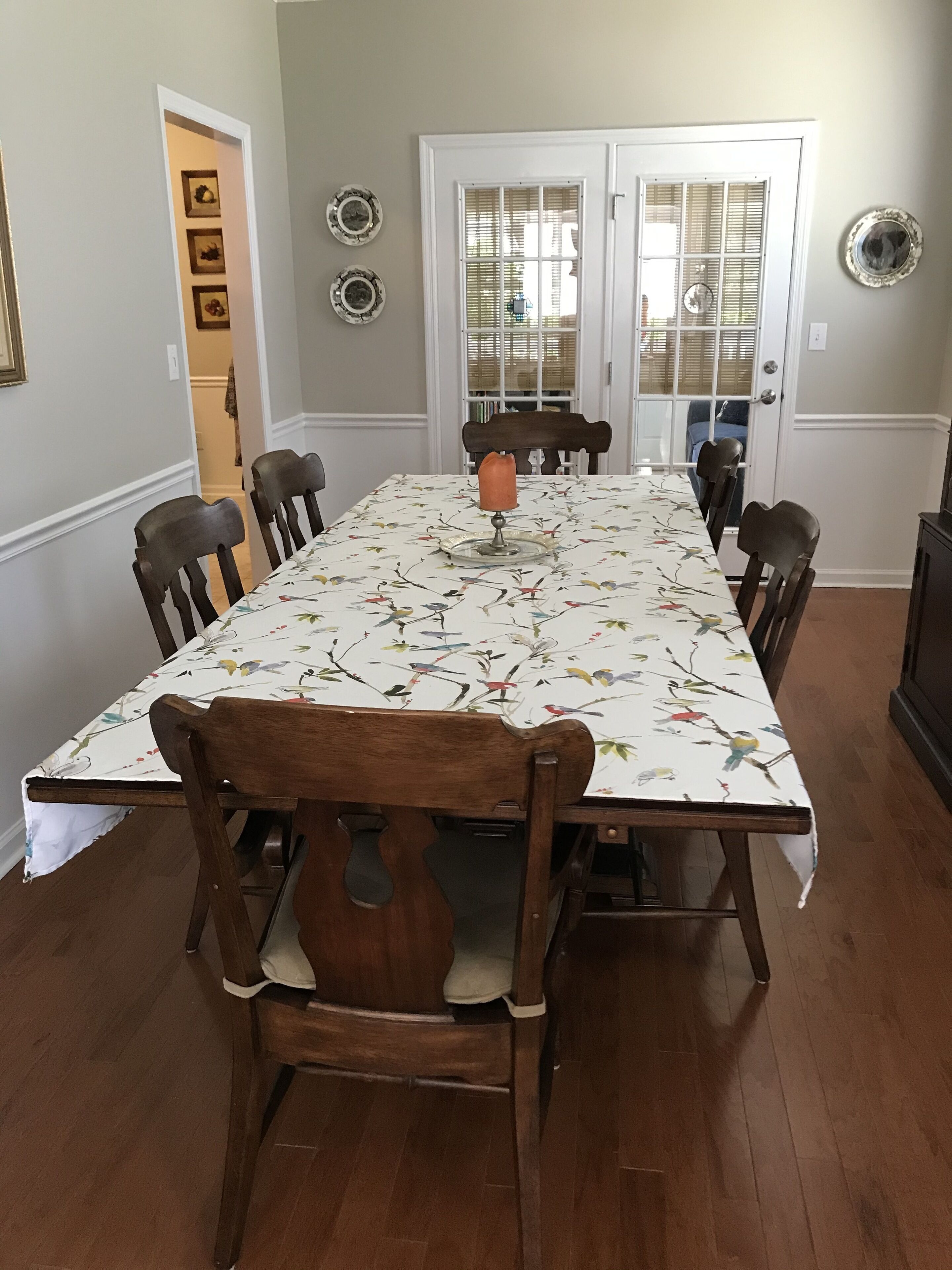 Een eetkamer met een lange tafel, houten stoelen en een tafelkleed met bloemen.