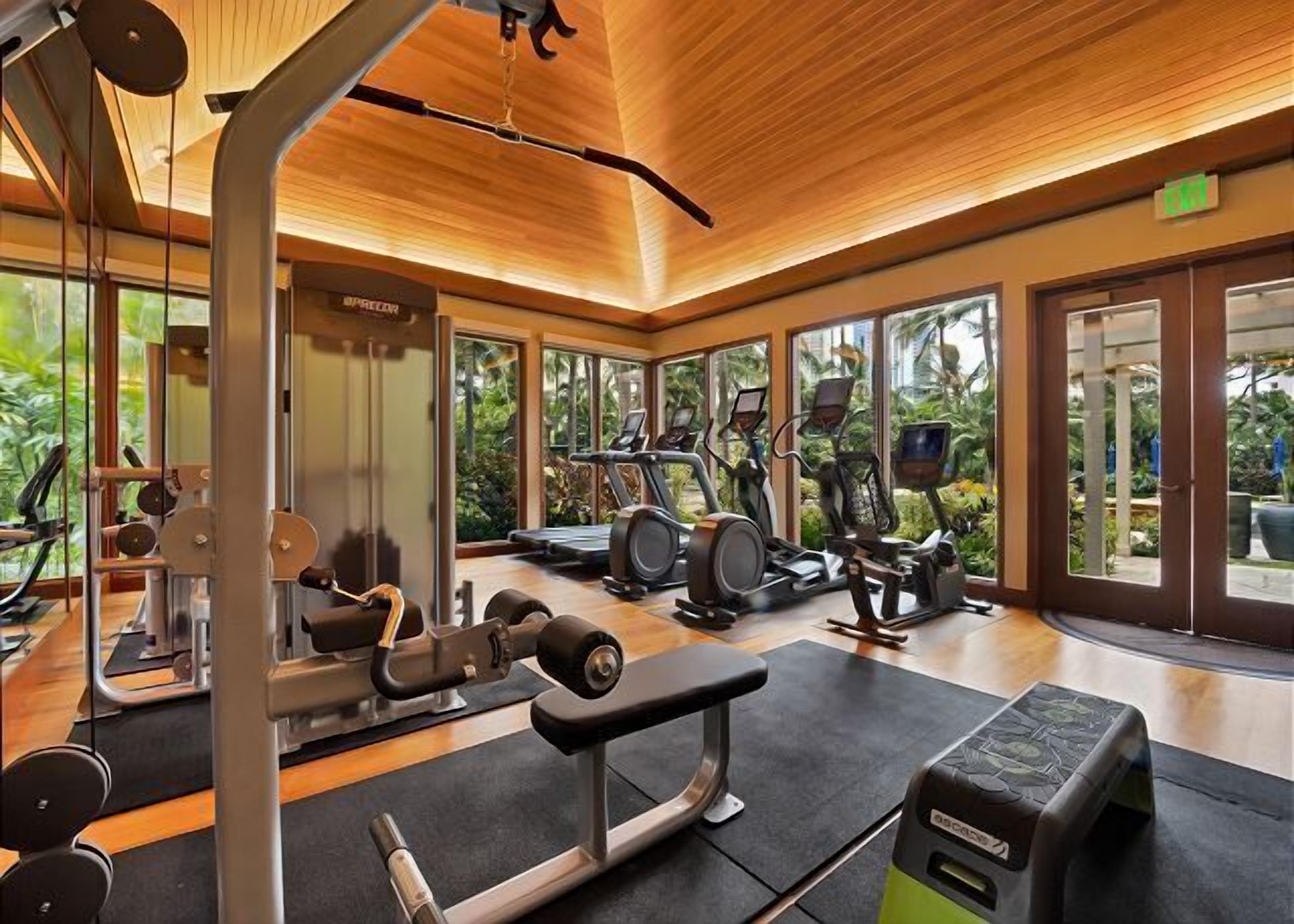 A gym with cardio machines, weight equipment, and large windows offering a view of greenery.