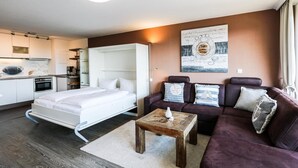 Una sala moderna con un sofá, una mesa de centro y una cama. Hay una zona de cocina con armarios y un refrigerador.