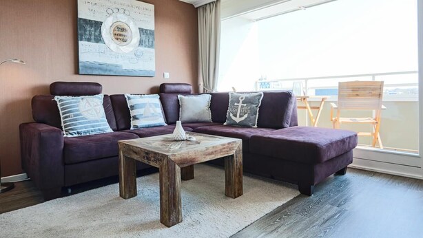 Una sala de estar moderna con un sofá morado oscuro, una mesa de centro de madera y un ventanal con vistas a la ciudad.