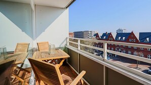 Un balcón con sillas y mesa de madera, con vistas a una hilera de casas rojas con marcos de ventanas blancos.