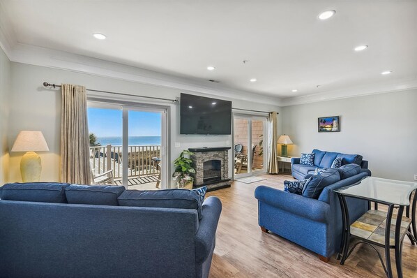 A living room with a TV, sofas, a fireplace, and a balcony with a view. - Atlantis Villas 102-6BR/5BA Oceanfront condo in Ocean Drive (North Myrtle Beach)