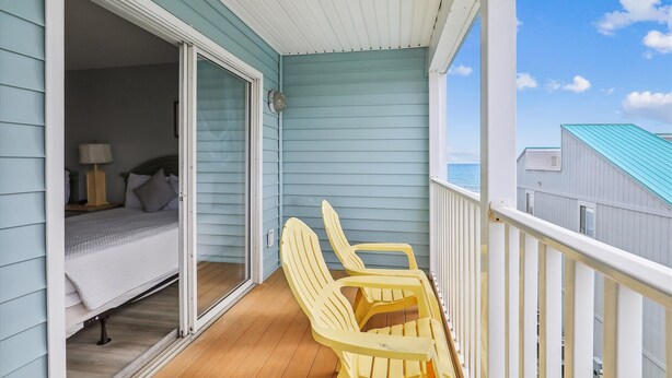 Een balkon met een bed en twee stoelen, met uitzicht op een wateroppervlak.