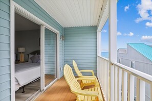 A balcony with a bed and two chairs, overlooking a body of water.