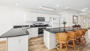 Een moderne keuken met witte kastjes, een zwart aanrecht en een centraal eiland met rieten stoelen.