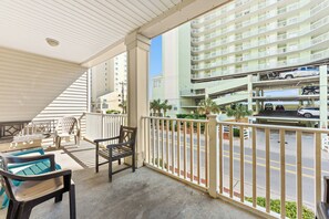 A balcony with outdoor furniture, a view of a multi-story parking garage, and a building with a light green facade.