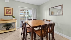 Un comedor con una mesa y sillas de madera, una consola con una planta y una ventana con cortinas.