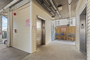 A commercial building with closed metal doors, a trash compactor, and a fenced area with shopping carts.