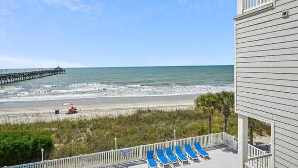 A beach view with a pier, lounge chairs, and a lifeguard sign.