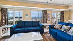 A living room with two blue sofas, a glass coffee table, and a ceiling fan.