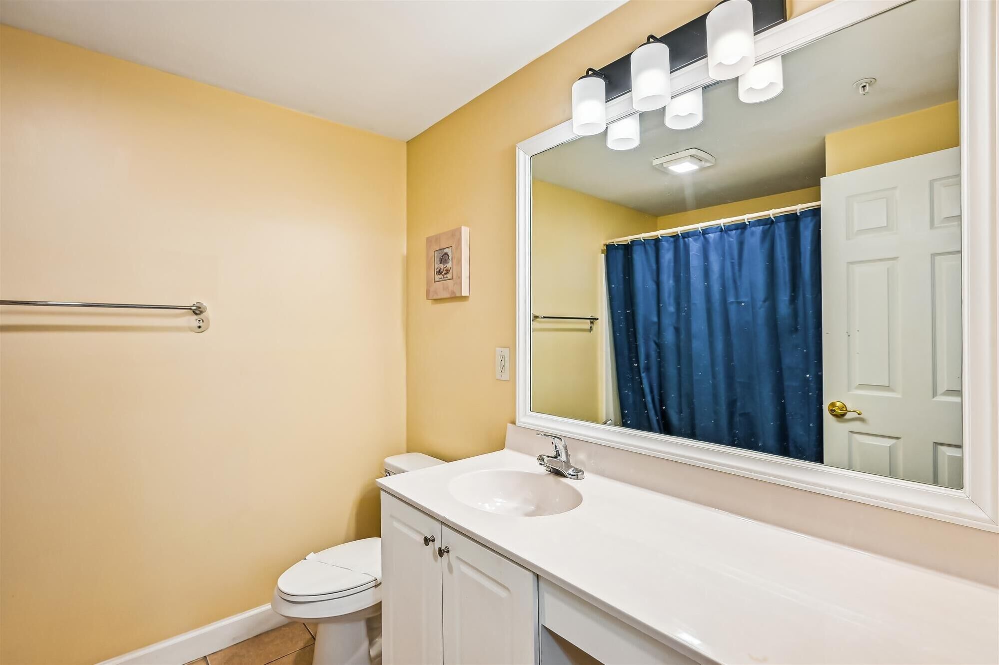 A bathroom with a white sink, a toilet, a large mirror, and a blue shower curtain.