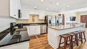 Una cocina moderna con armarios blancos, electrodomésticos de acero inoxidable, encimera de granito y taburetes de madera.