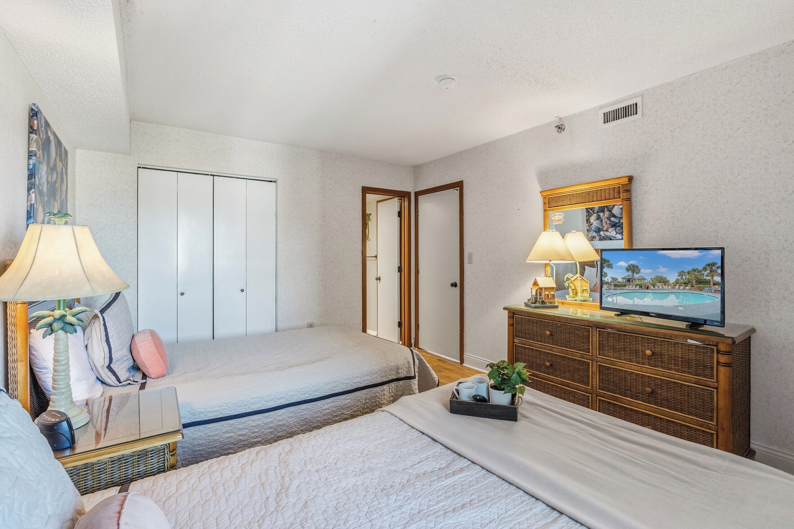 A hotel room with two beds, a television, a dresser, and a painting on the wall.
