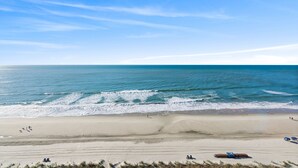 A beach with a clear sky, calm sea, and a few people and beach chairs.